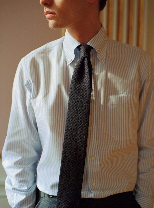 Person wearing a light blue striped shirt and dark tie indoors.