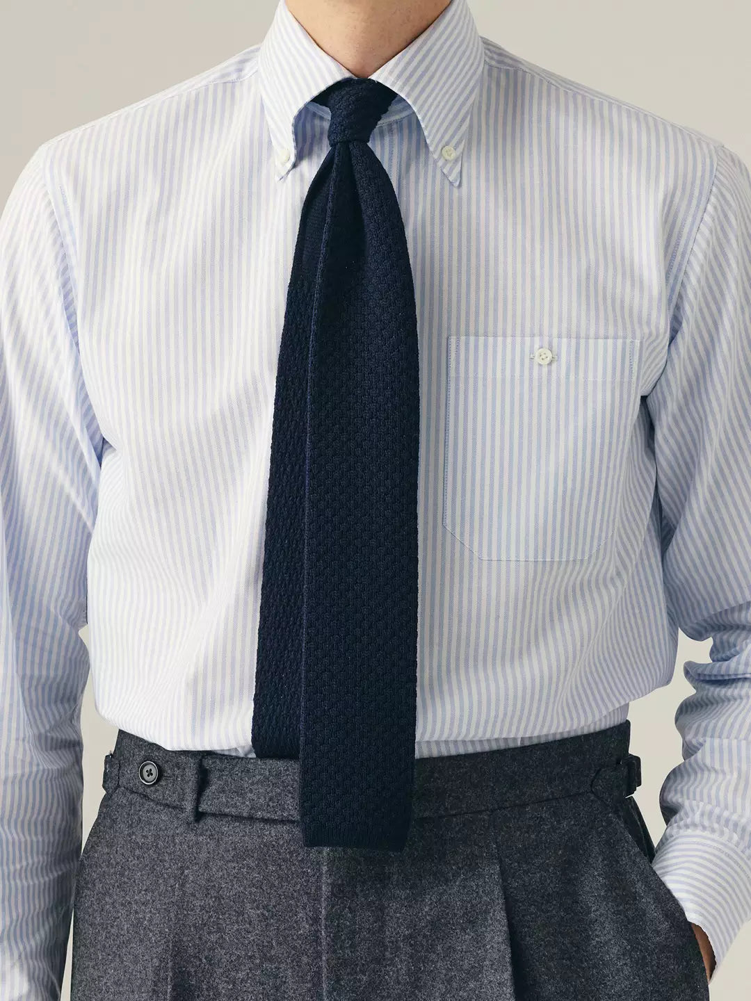 Person wearing a blue striped shirt, navy knitted tie, and grey trousers