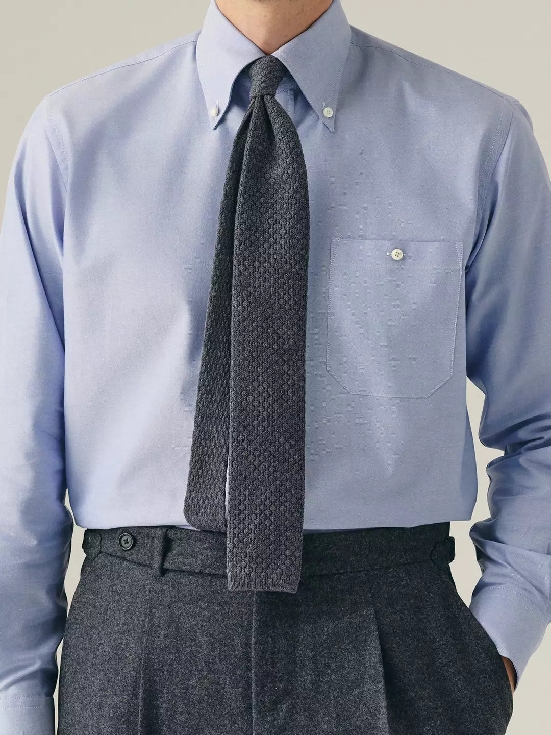 Light blue button down shirt with a grey tie and grey pleated trousers