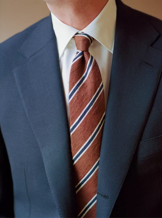 Man wearing a dark suit with a brown striped tie. 