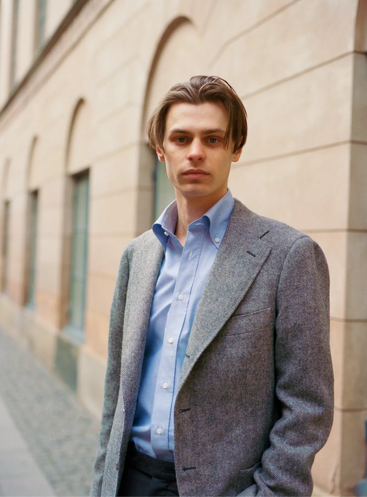 Man wearing a grey blazer over a light blue shirt against a beige building background