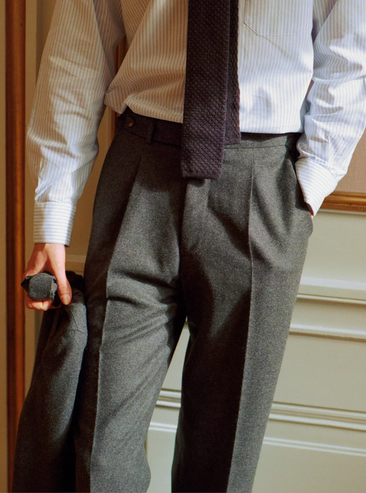 Person wearing a white shirt, dark tie, and grey trousers indoor.