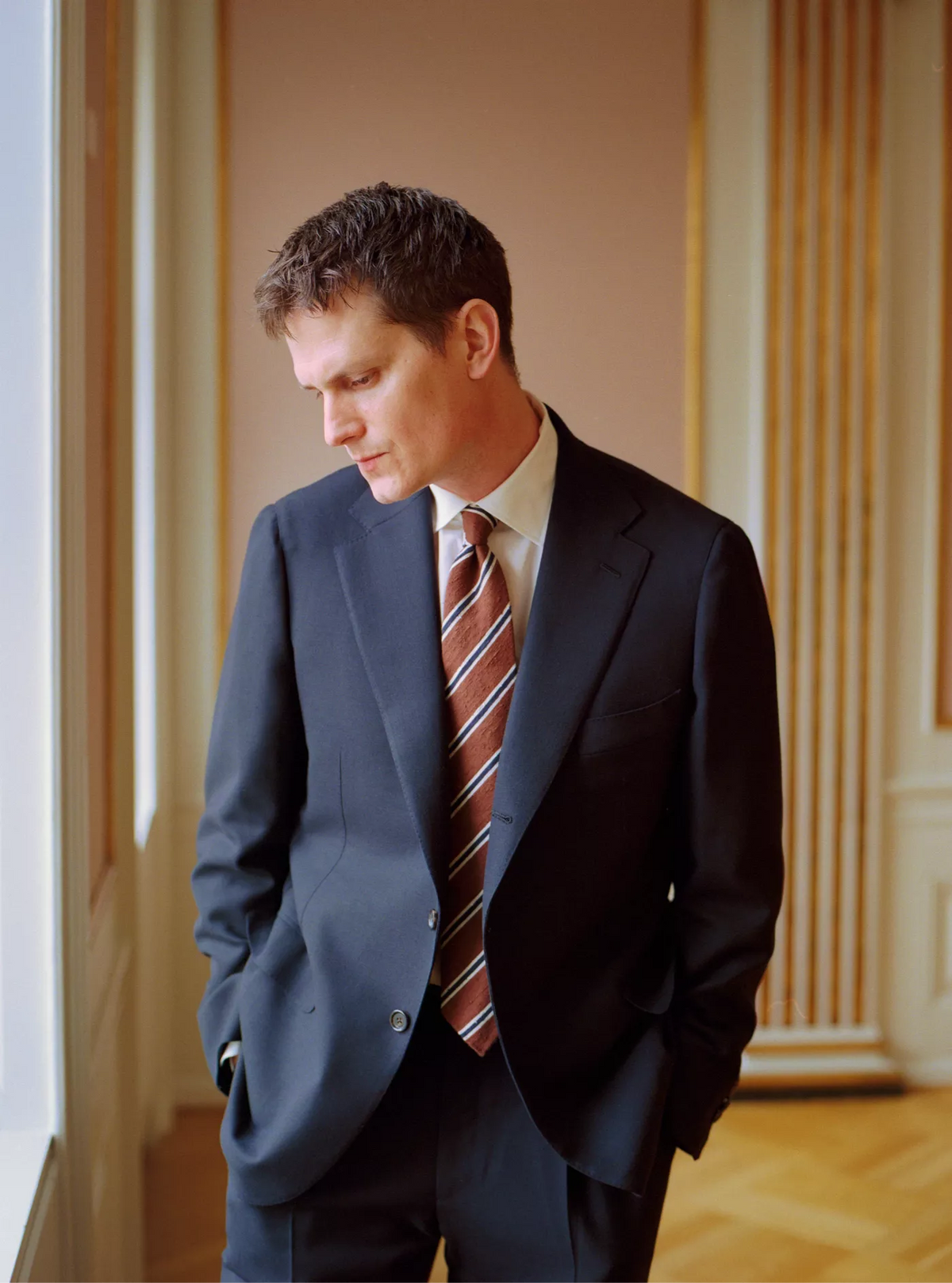 Man in a suit and tie standing in a room with wooden paneling