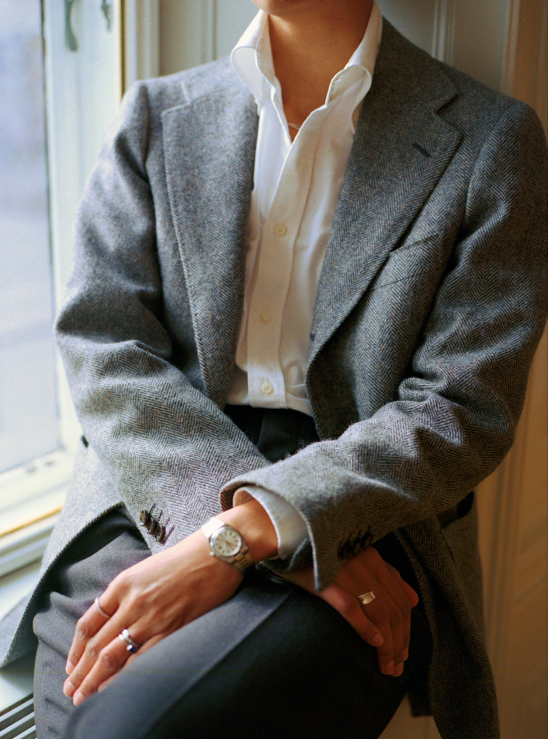 Person wearing a grey tweed blazer and white shirt sitting by a window.