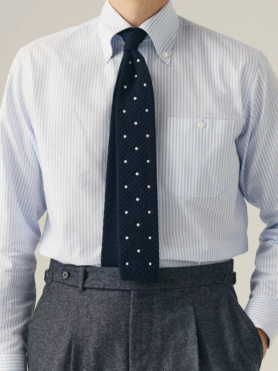 Person wearing a light blue striped shirt, dark tie, and gray trousers