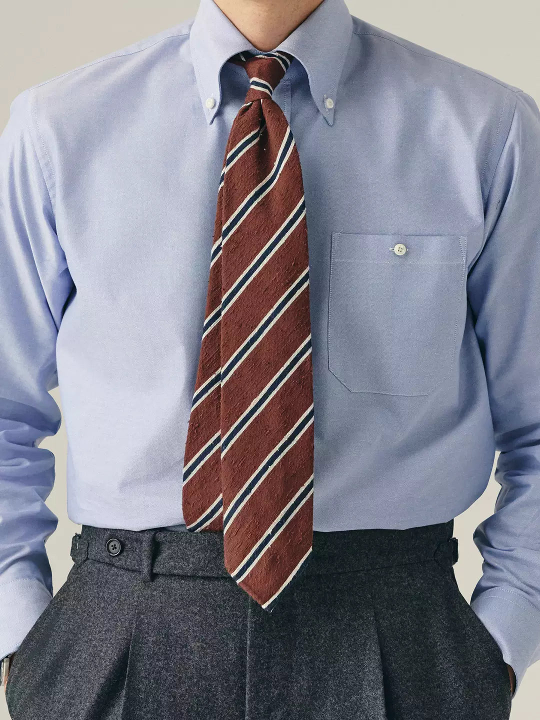 Person wearing a light blue dress shirt with a brown striped tie and gray pants.